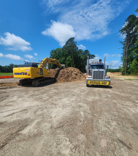 Komatsu excavator loading material beside a JW Hart Transport oversize load truck