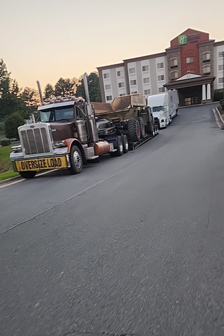 JW Hart Transport oversize load semi hauling a dump truck past a hotel at dusk