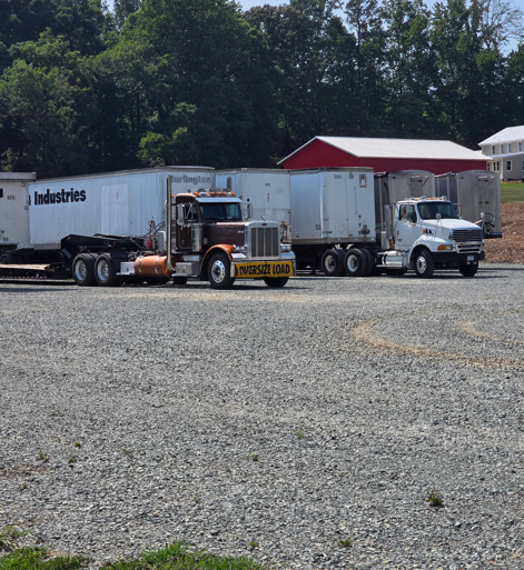 JW Hart Transport brown semi with oversize load banner parked in a truck lot beside dry vans