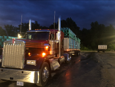 Red JW Hart Transport semi at night hauling a load of green pipe