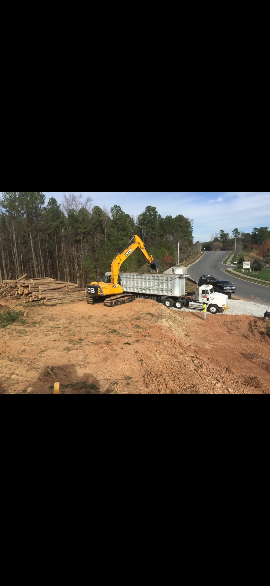 White JW Hart Transport truck receiving material from an excavator at a land-clearing site
