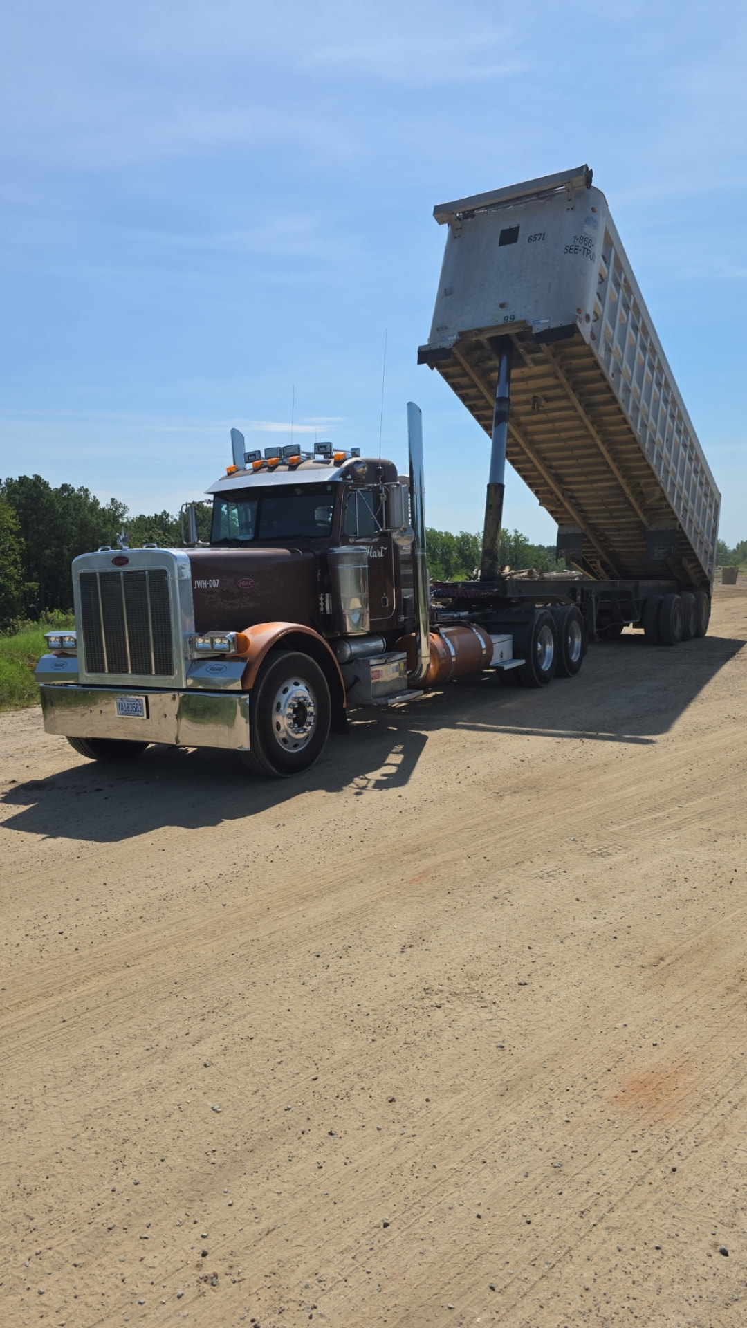 JW Hart Transport JWH-007 with raised silver dump trailer unloading on a dirt lot