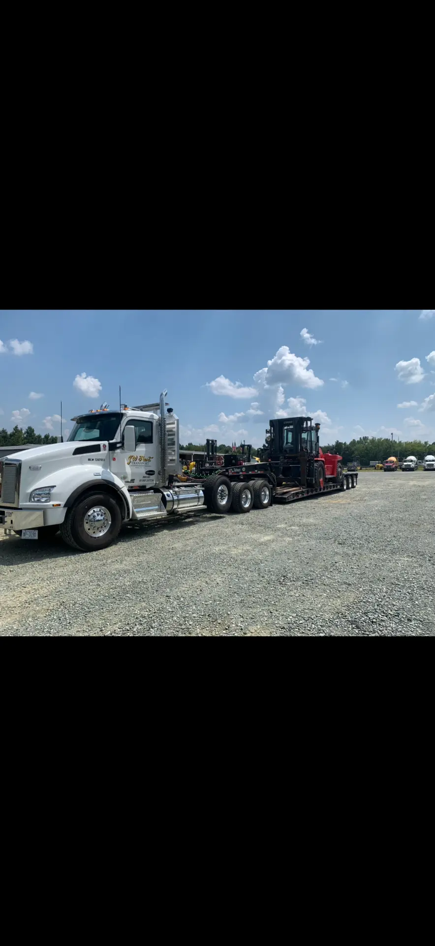 White JW Hart Transport semi hauling material handling equipment across a gravel yard