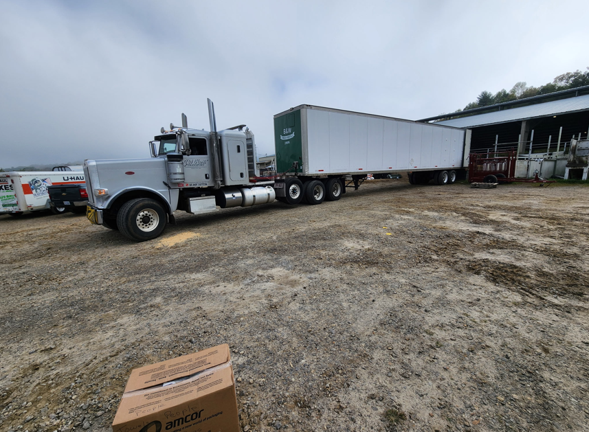 Silver JW Hart Transport semi hooked to a long green B&W trailer at a farm