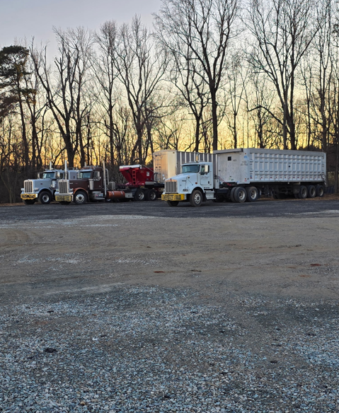 JW Hart Transport fleet parked at sunset with dump trailers and semi trucks