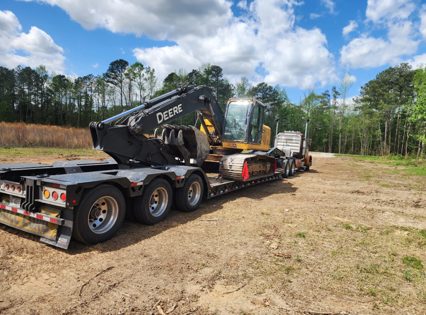 John Deere excavator secured on a lowboy trailer at a rural jobsite