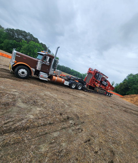 JW Hart Transport truck hauling forestry equipment on a lowboy trailer