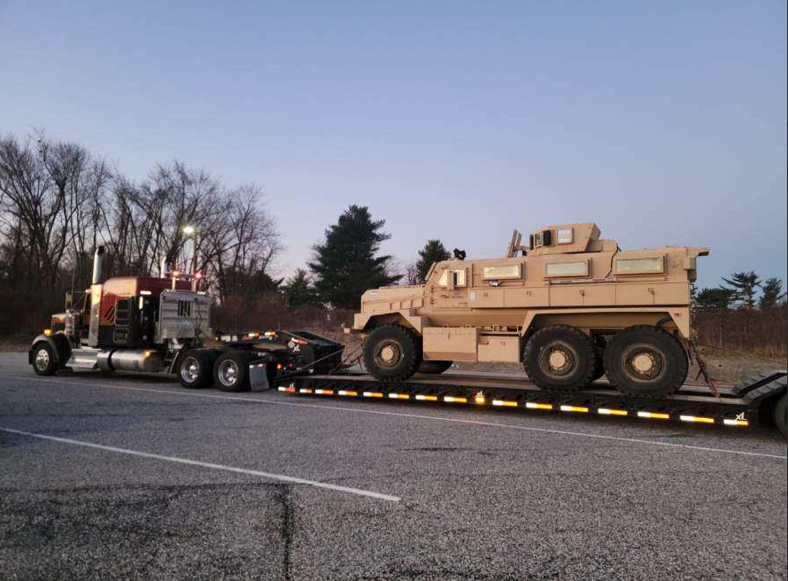 JW Hart Transport semi hauling an armored military vehicle on a lowboy trailer at dusk