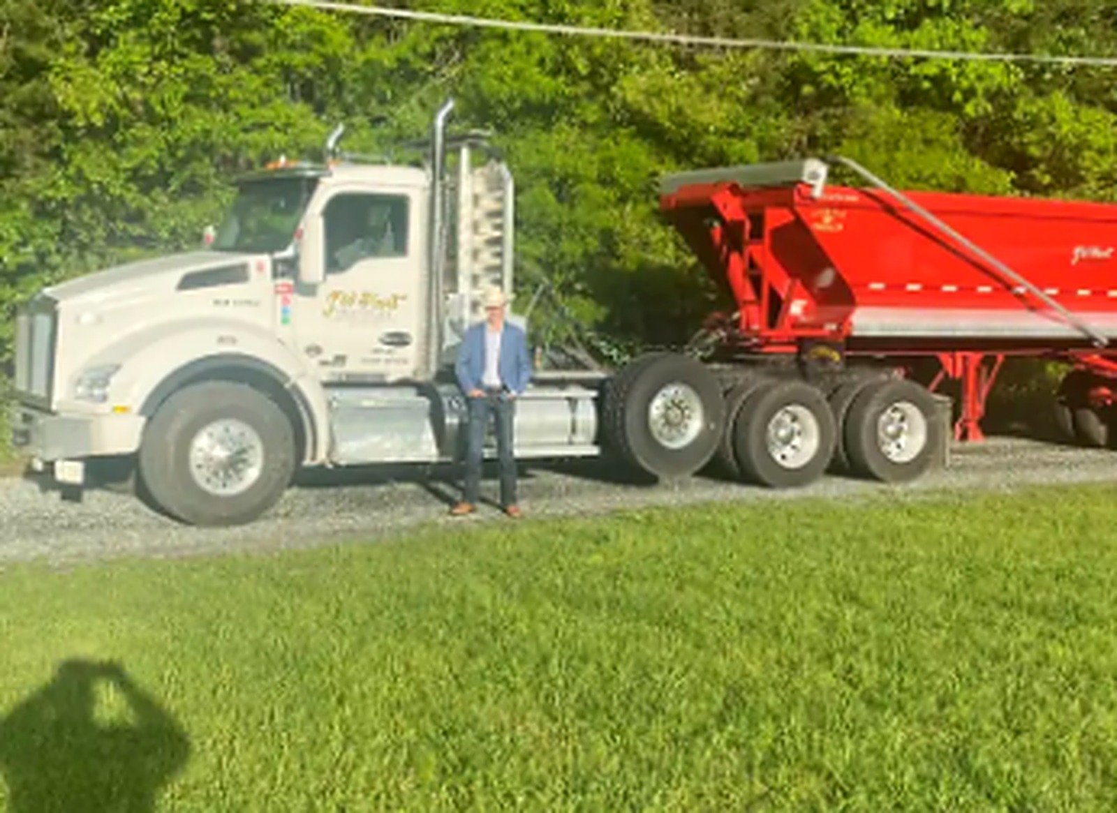 White JW Hart Transport semi with red dump trailer at a grassy jobsite