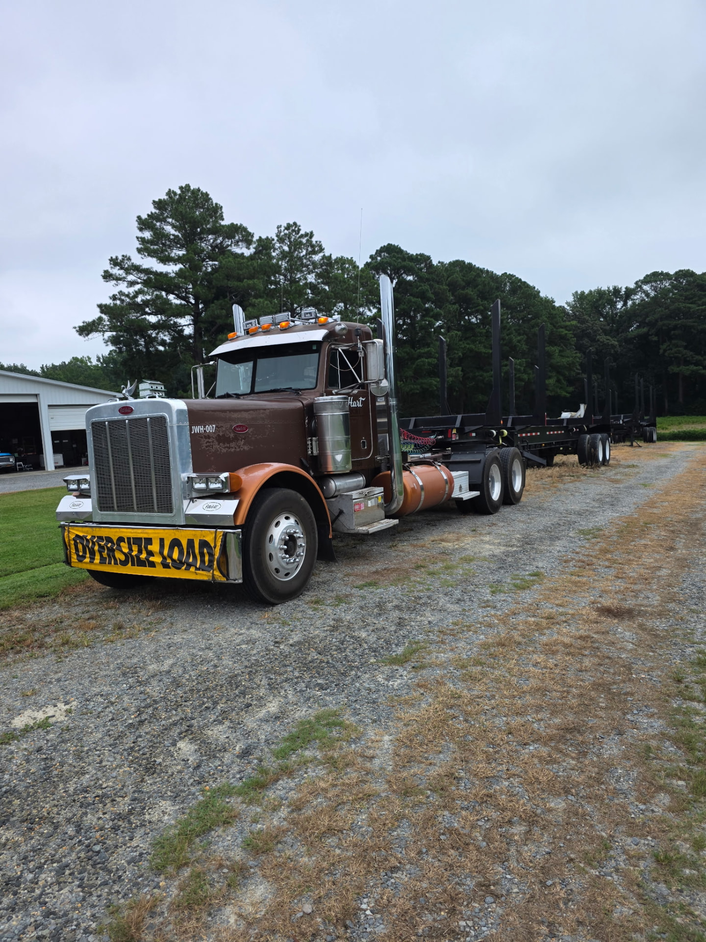 JW Hart Transport JWH-007 brown semi with empty log trailer near a white shop building