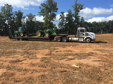 JW Hart Transport semi hauling two green John Deere tractors on a flatbed trailer