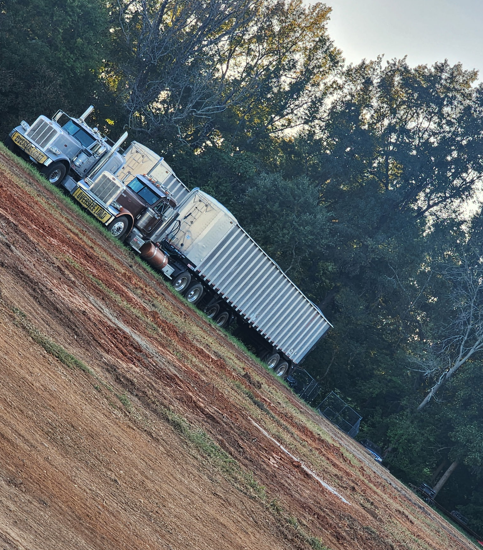 JW Hart Transport trucks lined up on a red-clay lot with a long silver trailer