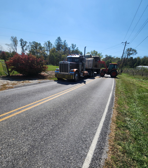 JW Hart Transport oversize load semi hauling a red tractor on a two-lane country road