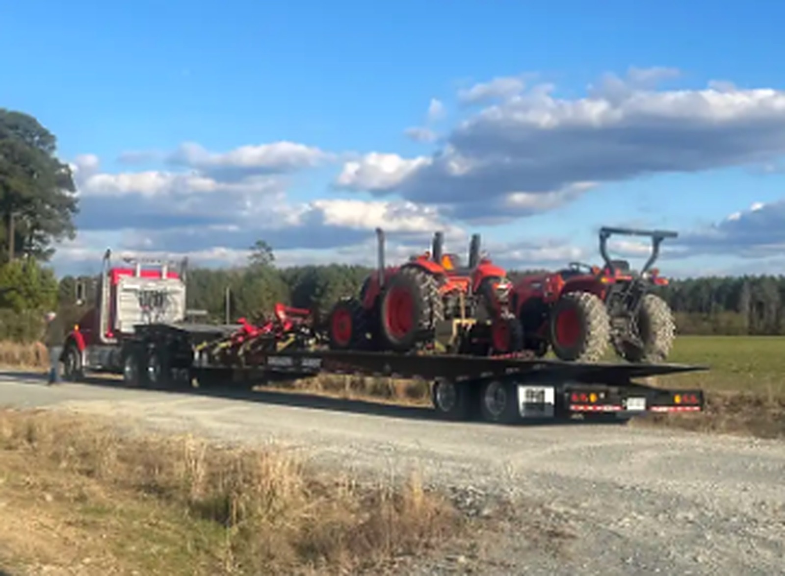 JW Hart Transport semi hauling multiple red tractors on a flatbed trailer
