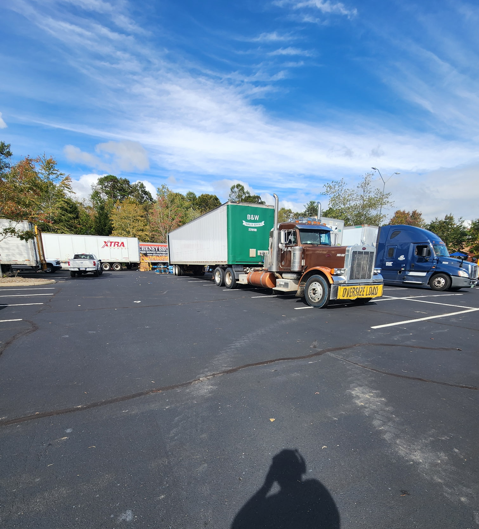JW Hart Transport semi with oversize load banner hauling a green B&W trailer in a truck lot