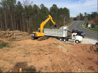 Yellow excavator loading a JW Hart Transport dump trailer at a jobsite