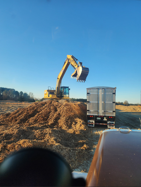 Excavator loading mulch into a JW Hart Transport trailer