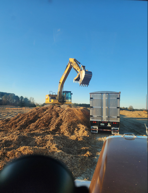 Excavator loading material into a JW Hart Transport dump trailer at a construction site