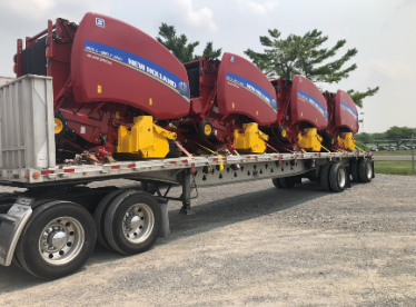 Flatbed trailer loaded with red New Holland hay equipment