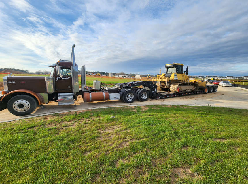 JW Hart Transport truck hauling a yellow bulldozer on a lowboy trailer at a North Carolina jobsite