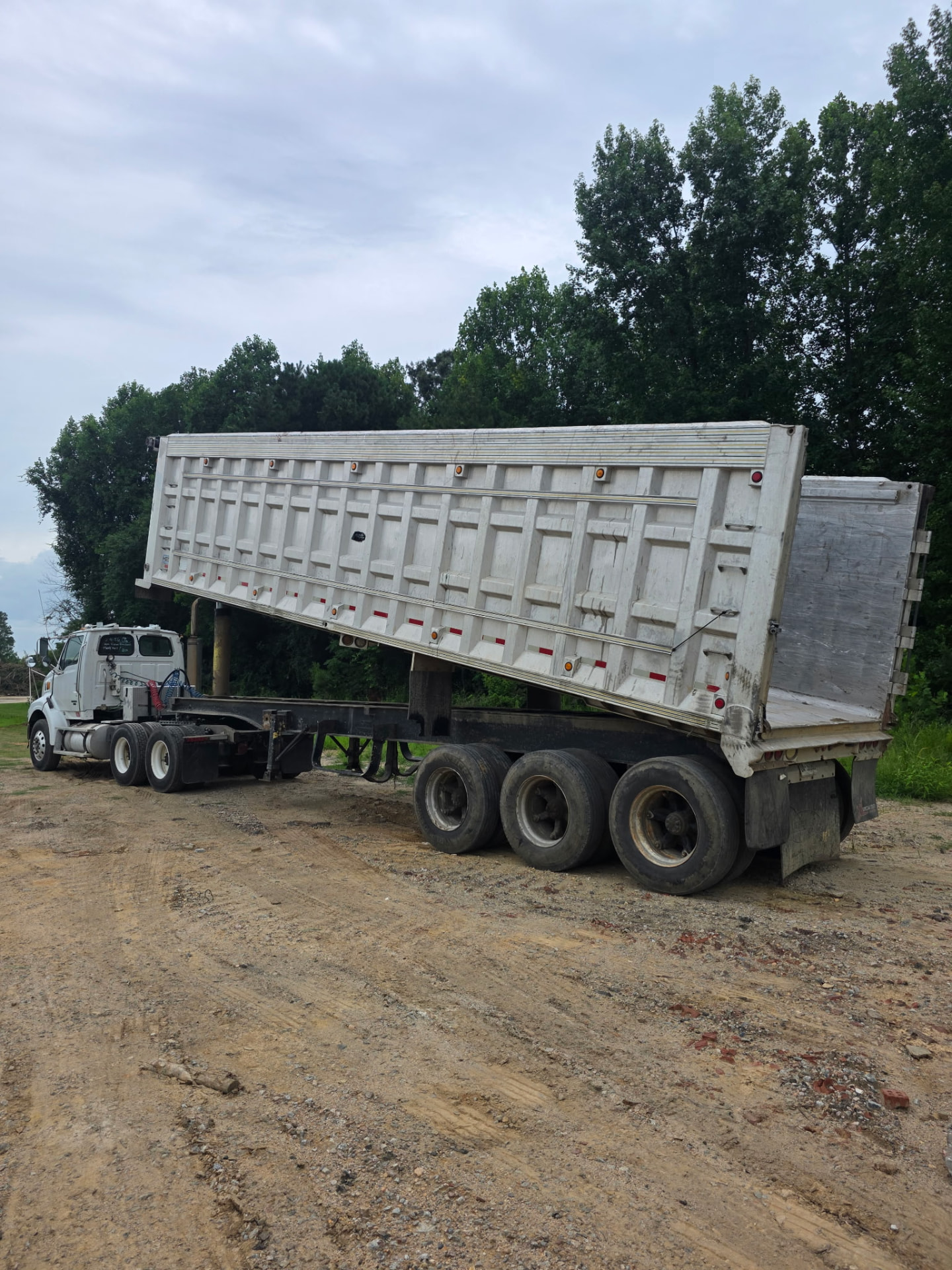Long white dump trailer raised high behind a JW Hart Transport tractor