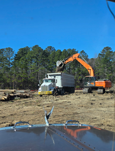 Orange excavator loading a JW Hart Transport dump trailer at a forestry jobsite