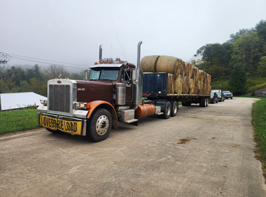 JW Hart Transport semi hauling round hay bales on a flatbed trailer down a rural road