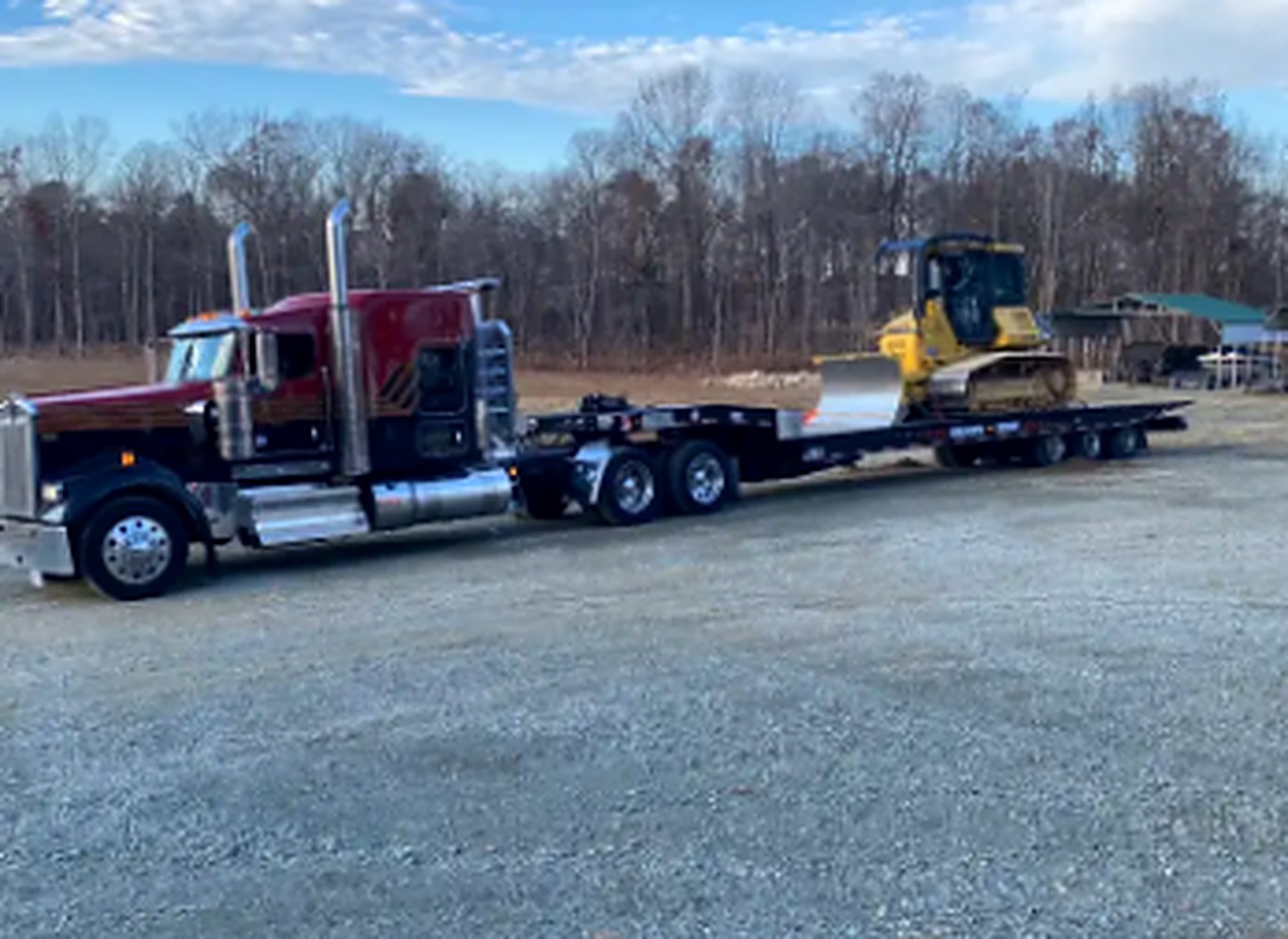 Red JW Hart Transport semi hauling a yellow bulldozer on a lowboy trailer